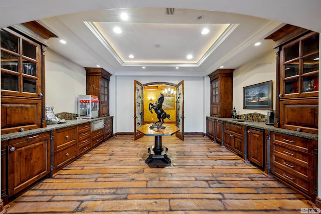 kitchen with a raised ceiling, dark stone countertops, light hardwood / wood-style floors, and crown molding