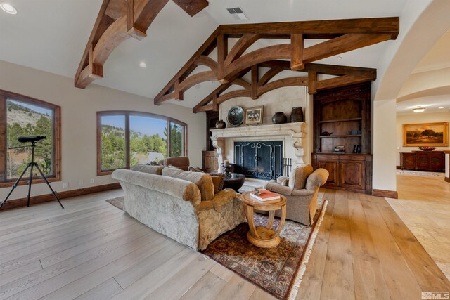 living room with a premium fireplace, light hardwood / wood-style flooring, high vaulted ceiling, and beamed ceiling