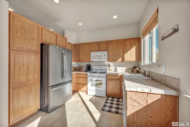 kitchen with white appliances, tile countertops, and sink