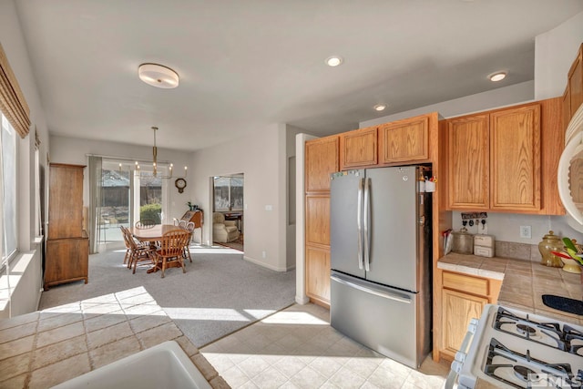 kitchen featuring tile counters, decorative light fixtures, stainless steel fridge, white range with gas cooktop, and light colored carpet