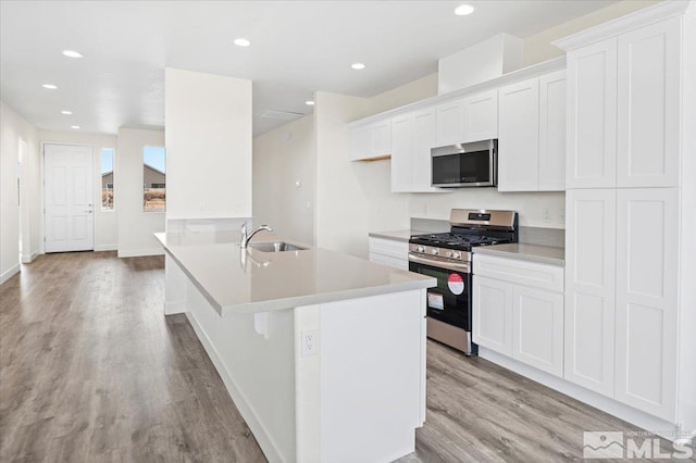 kitchen with stainless steel appliances, white cabinets, sink, and light hardwood / wood-style flooring