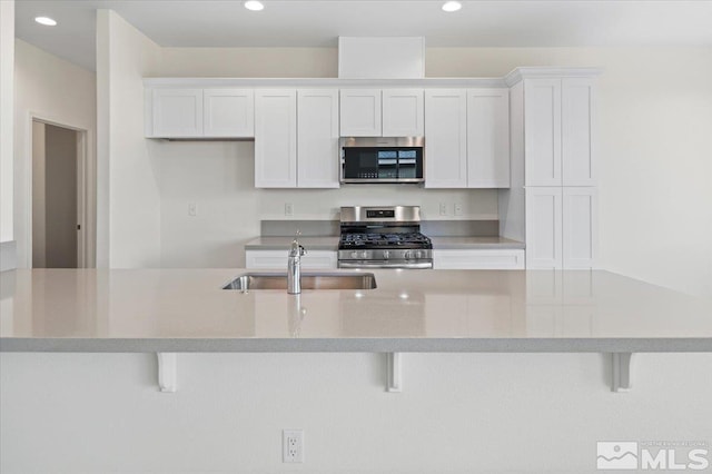 kitchen featuring appliances with stainless steel finishes, a kitchen breakfast bar, white cabinetry, and sink