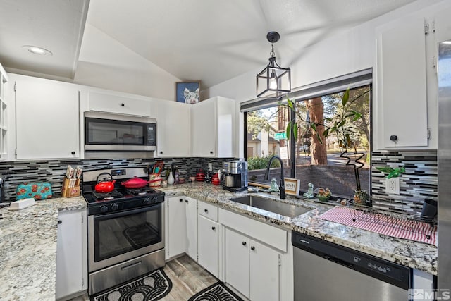 kitchen featuring stainless steel appliances, hanging light fixtures, light stone countertops, sink, and white cabinetry