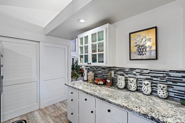 kitchen featuring white cabinets, light wood-type flooring, light stone countertops, and decorative backsplash