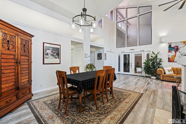 dining area with light hardwood / wood-style floors, french doors, a towering ceiling, and ceiling fan with notable chandelier