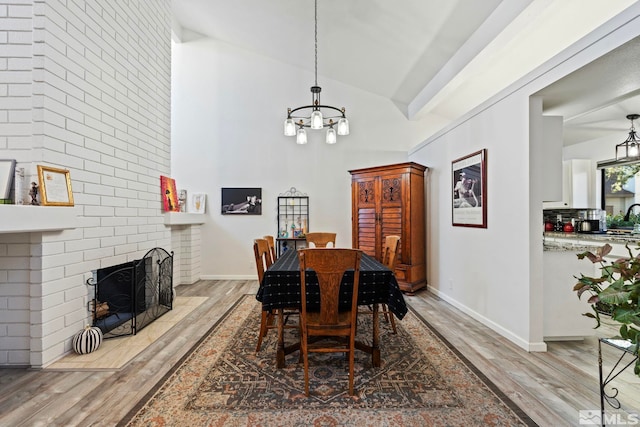 dining space featuring hardwood / wood-style floors, a notable chandelier, a brick fireplace, and high vaulted ceiling