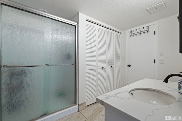 bathroom with a textured ceiling, tile patterned flooring, vanity, and a shower with shower door