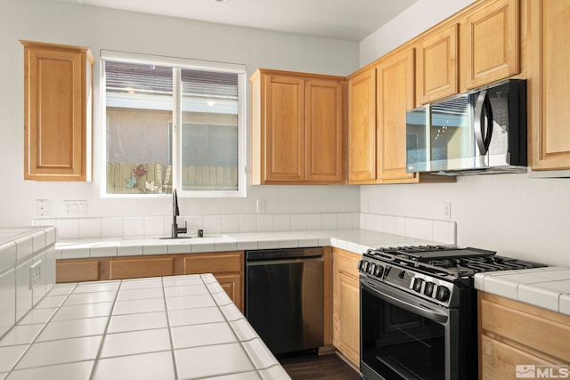 kitchen featuring gas range oven, tile countertops, sink, black dishwasher, and light brown cabinets