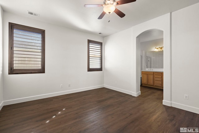 unfurnished bedroom featuring ensuite bath, dark wood-type flooring, and ceiling fan