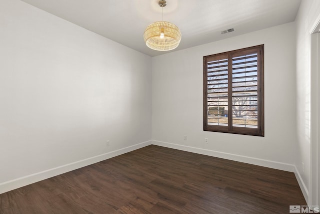 spare room with dark hardwood / wood-style flooring and a chandelier