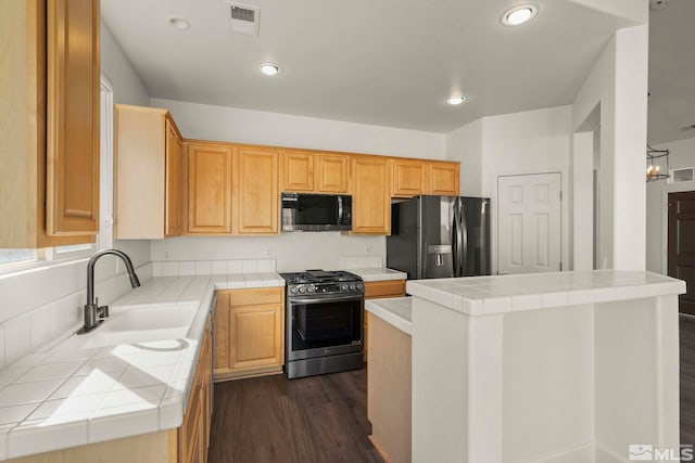 kitchen featuring sink, a center island, stainless steel gas range, black fridge, and tile counters