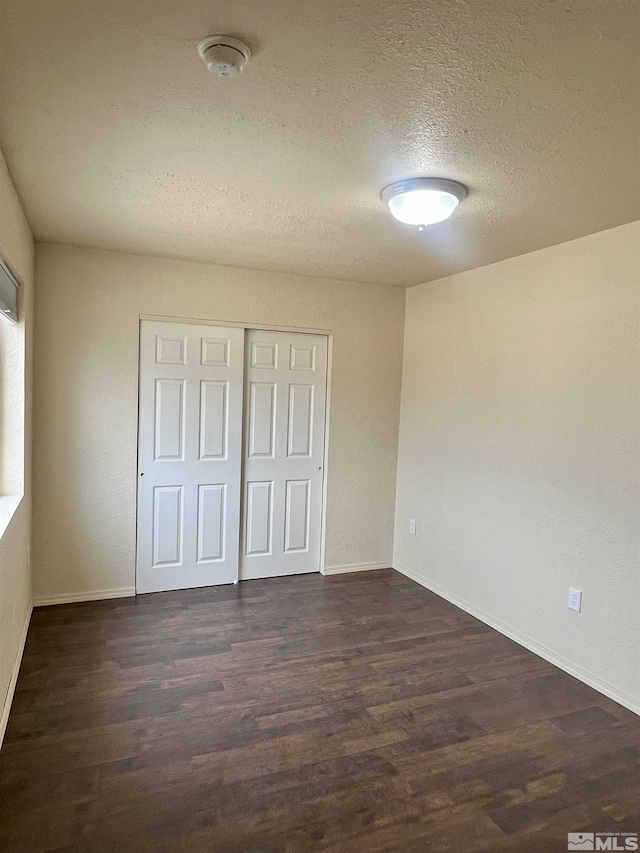 unfurnished bedroom featuring a textured ceiling, dark wood-type flooring, and a closet