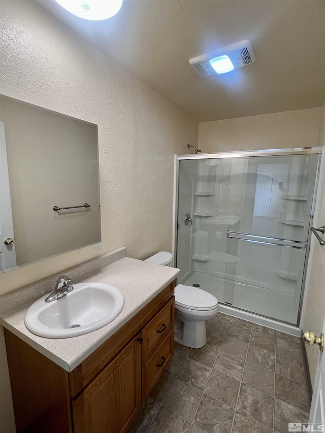 bathroom featuring toilet, vanity, a textured ceiling, and a shower with shower door