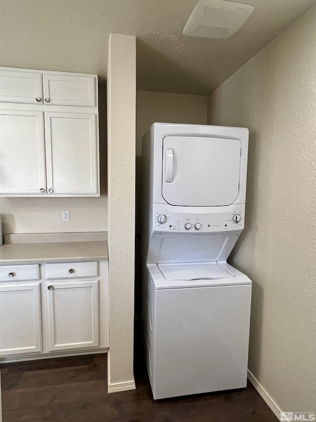 clothes washing area featuring stacked washer and clothes dryer, cabinets, and dark hardwood / wood-style floors