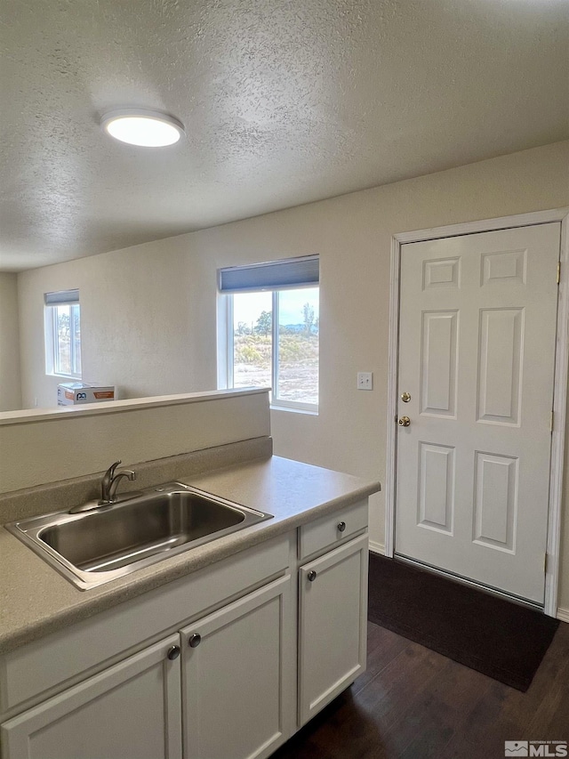 kitchen with dark wood-type flooring, a textured ceiling, white cabinetry, and sink