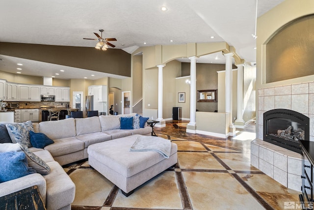 living room featuring a tile fireplace, ceiling fan, vaulted ceiling, and decorative columns