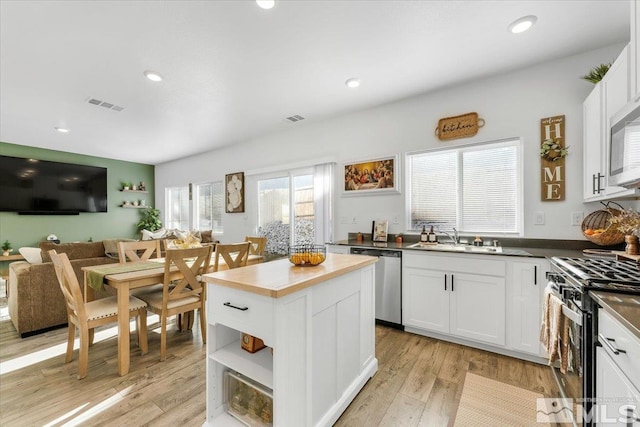 kitchen with a center island, stainless steel appliances, light wood-type flooring, white cabinets, and sink