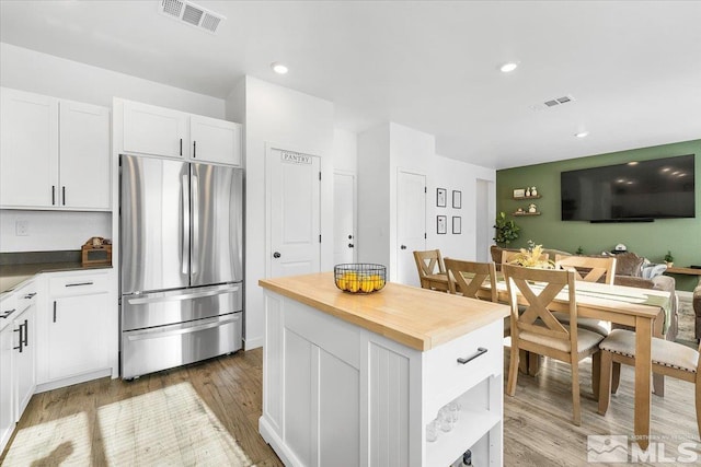 kitchen featuring white cabinetry, hardwood / wood-style floors, wood counters, and stainless steel fridge