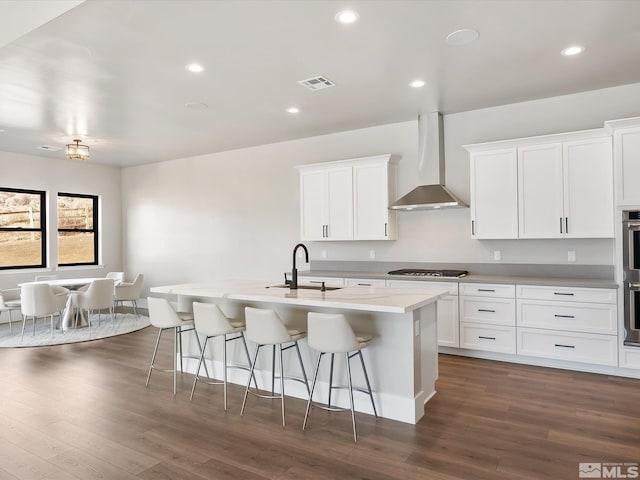 kitchen with stainless steel appliances, white cabinets, a kitchen island with sink, and wall chimney exhaust hood