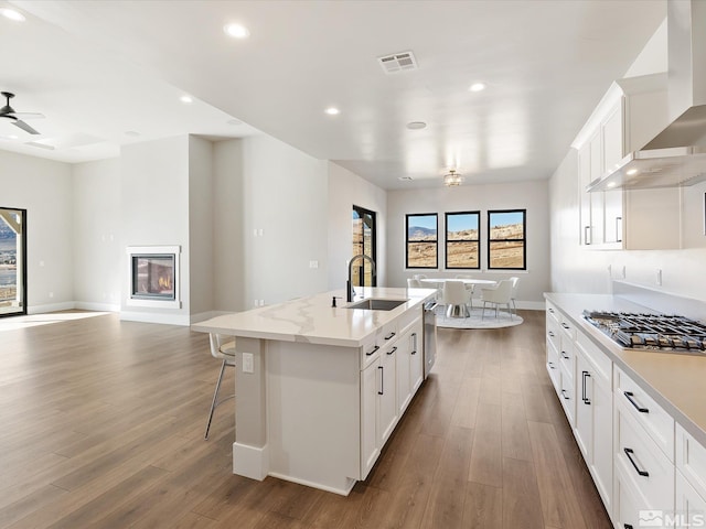 kitchen featuring sink, white cabinetry, wall chimney range hood, and a kitchen island with sink