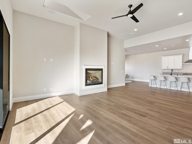 unfurnished living room with light hardwood / wood-style floors, ceiling fan, and vaulted ceiling