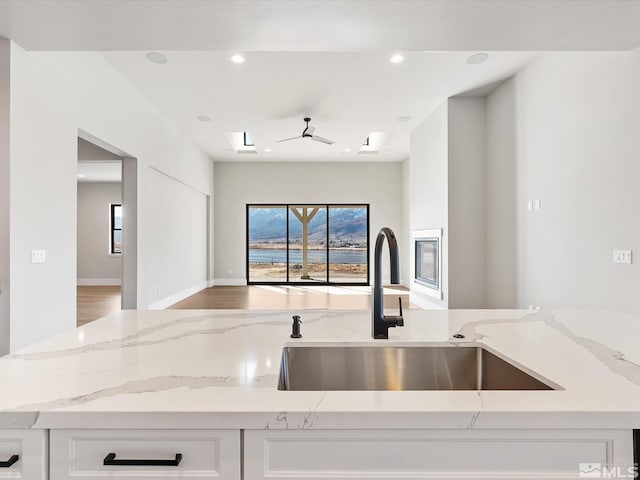 kitchen featuring sink, white cabinetry, a skylight, and light stone counters