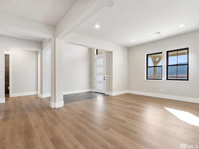 unfurnished living room with light wood-type flooring and beam ceiling