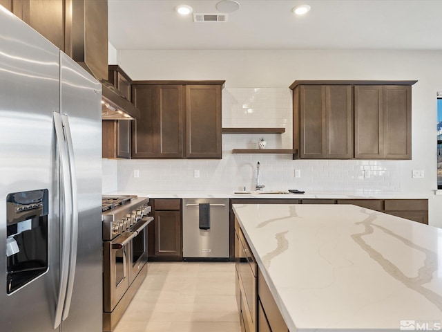 kitchen with appliances with stainless steel finishes, light stone countertops, light tile patterned floors, sink, and dark brown cabinets