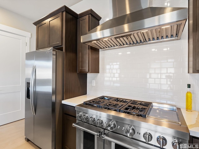 kitchen with range hood, light hardwood / wood-style floors, backsplash, appliances with stainless steel finishes, and dark brown cabinetry