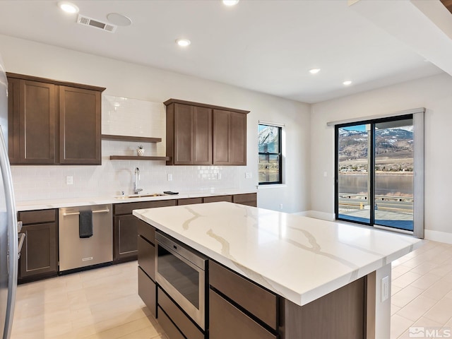 kitchen with stainless steel appliances, sink, light stone countertops, decorative backsplash, and dark brown cabinetry