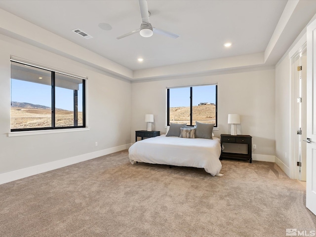 carpeted bedroom with ceiling fan, a tray ceiling, and a mountain view