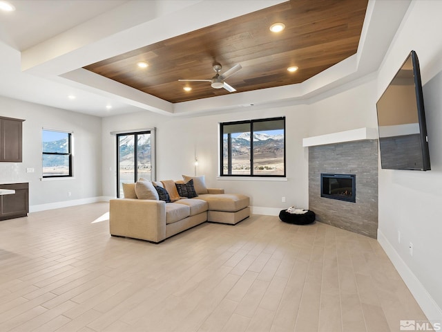 living room with wooden ceiling, ceiling fan, a tile fireplace, and a raised ceiling