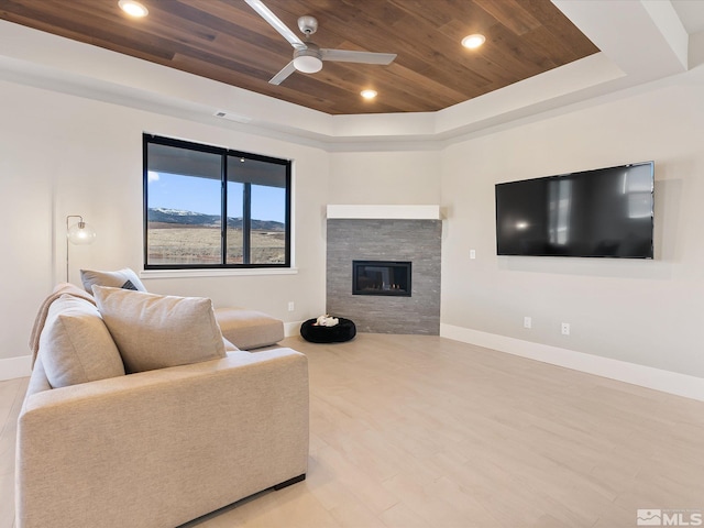 living room with wooden ceiling, light hardwood / wood-style floors, ceiling fan, a fireplace, and a tray ceiling