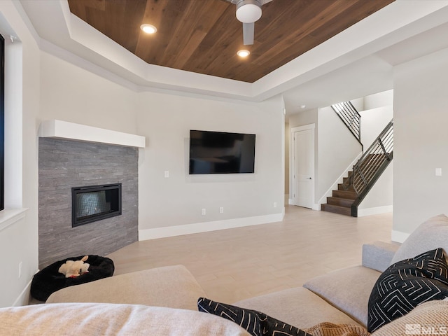 living room with a fireplace, ceiling fan, a tray ceiling, and wood ceiling