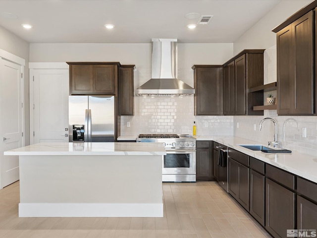 kitchen with stainless steel appliances, wall chimney range hood, a kitchen island, backsplash, and sink