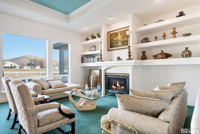 carpeted living room featuring ornamental molding, a tray ceiling, built in features, and a mountain view