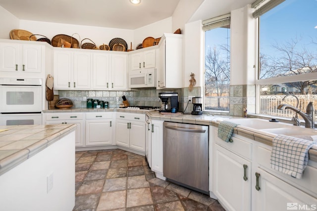 kitchen featuring white appliances, tile counters, white cabinets, backsplash, and sink