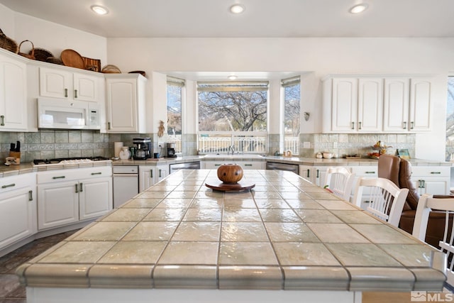 kitchen featuring white appliances, a center island, tile countertops, and white cabinets