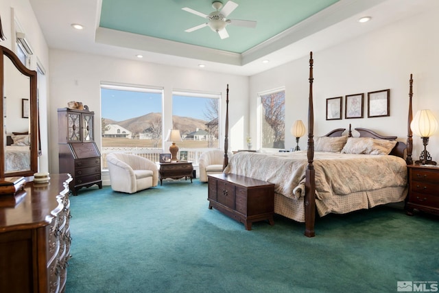 bedroom featuring a mountain view, ceiling fan, a tray ceiling, and dark colored carpet