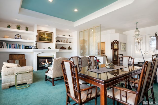 carpeted dining room with a raised ceiling and built in shelves