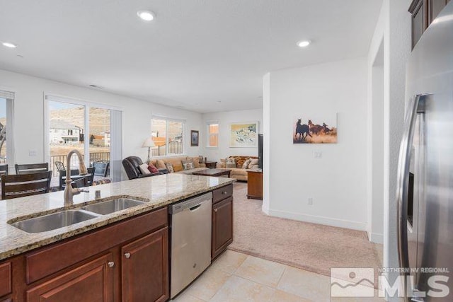 kitchen with light stone counters, sink, light carpet, and stainless steel appliances