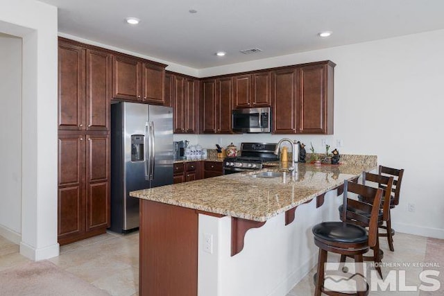 kitchen featuring appliances with stainless steel finishes, sink, kitchen peninsula, light stone counters, and a breakfast bar