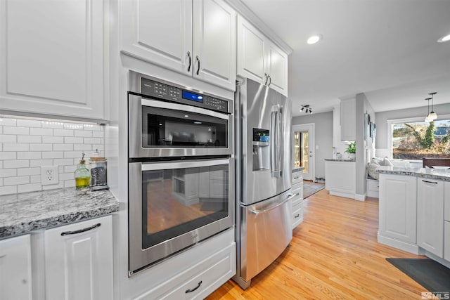 kitchen with stainless steel appliances, decorative backsplash, white cabinets, hanging light fixtures, and light hardwood / wood-style flooring