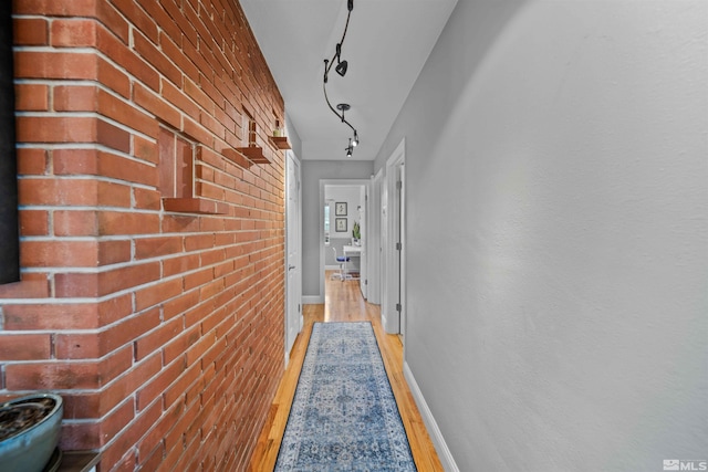 hall featuring light hardwood / wood-style floors, rail lighting, and brick wall