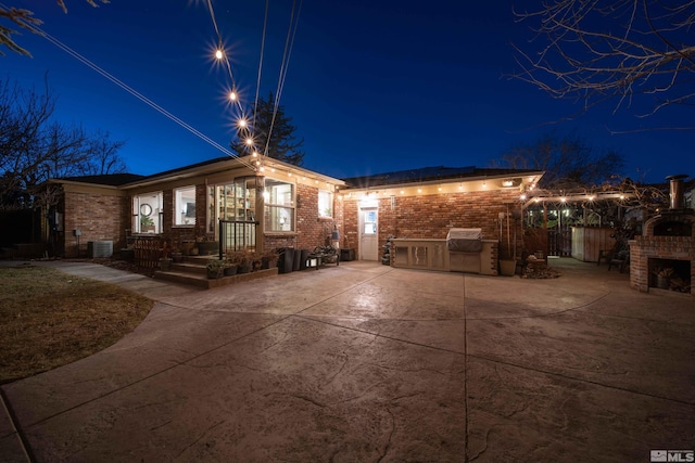 back house at night featuring central AC, a fireplace, and a patio