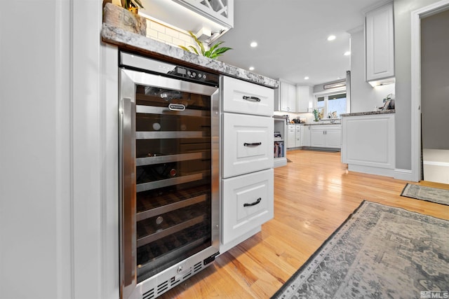 kitchen with light hardwood / wood-style floors, white cabinets, stone counters, and wine cooler