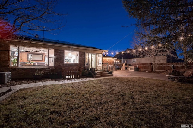 back house at twilight with central air condition unit, a patio, and a yard