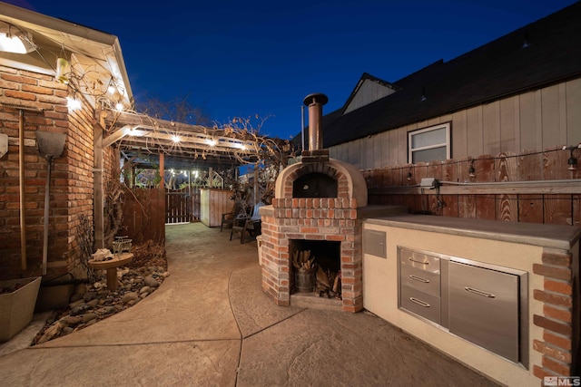 patio at night featuring an outdoor brick fireplace