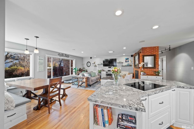 kitchen with light stone countertops, white cabinets, black electric stovetop, hanging light fixtures, and light wood-type flooring