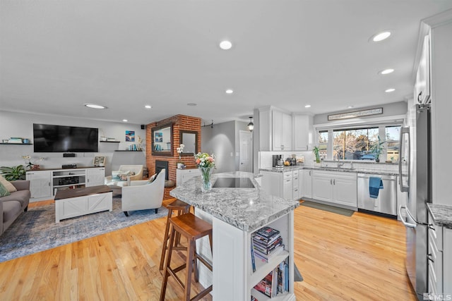 kitchen featuring white cabinetry, a kitchen bar, appliances with stainless steel finishes, light stone countertops, and sink